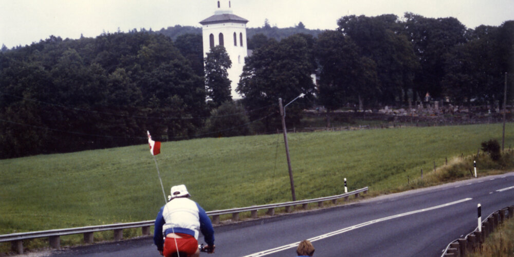 Rick Hansen wheeling towards a chapel accompanied by Lee Gibson, in Sweden during August of 1985.