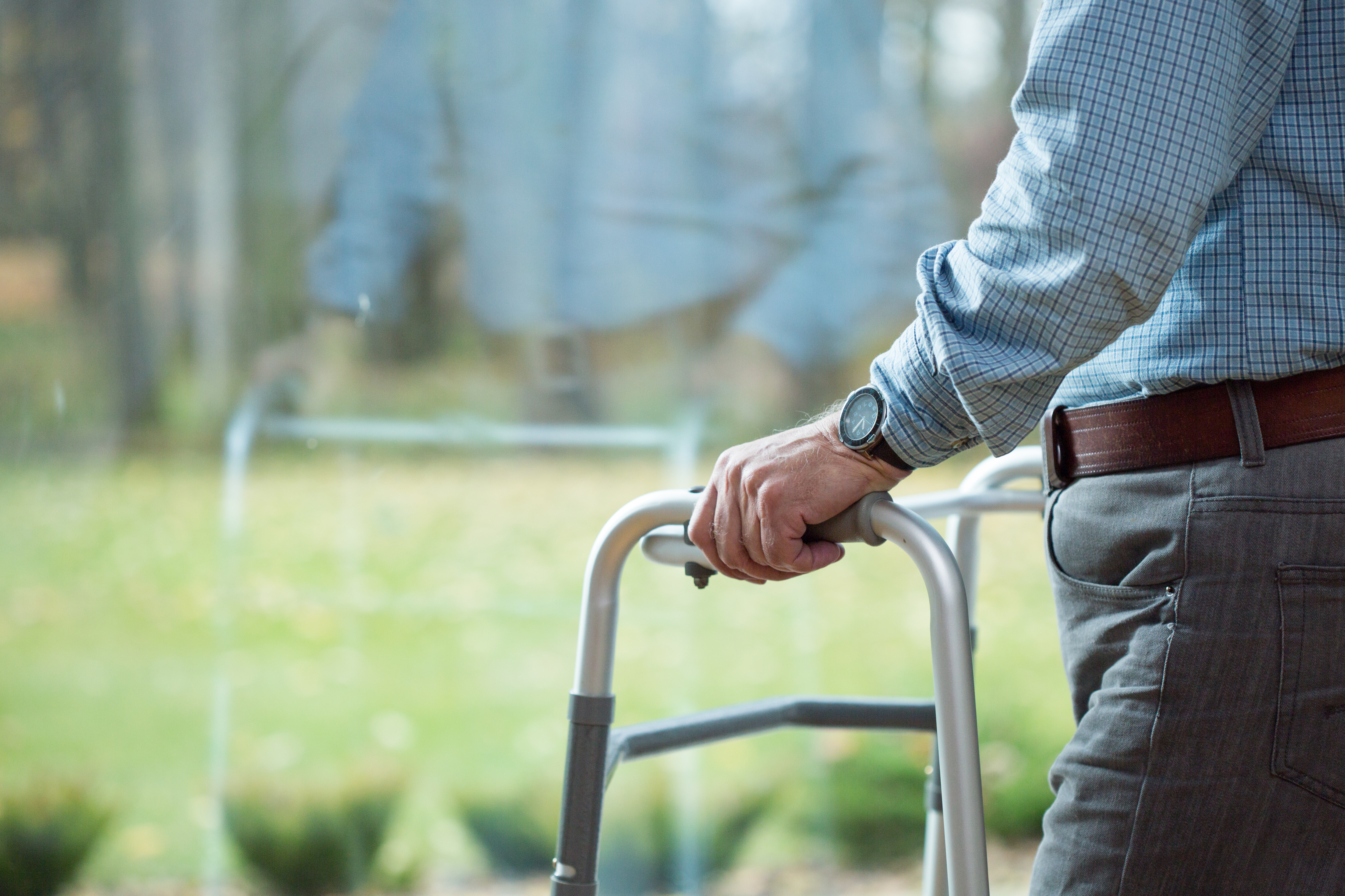 Close-up of a person standing indoors, holding a silver walker with both hands.
