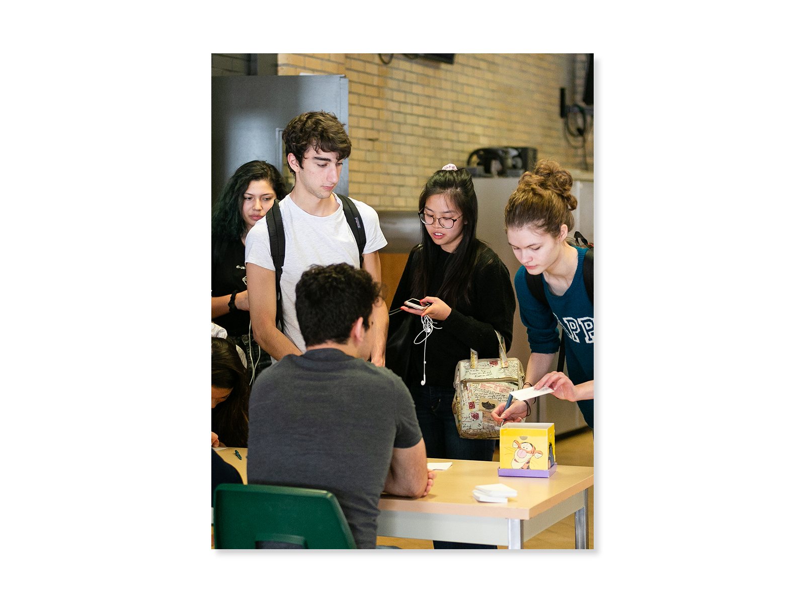 Four high school students gather at a table where another student is sitting.