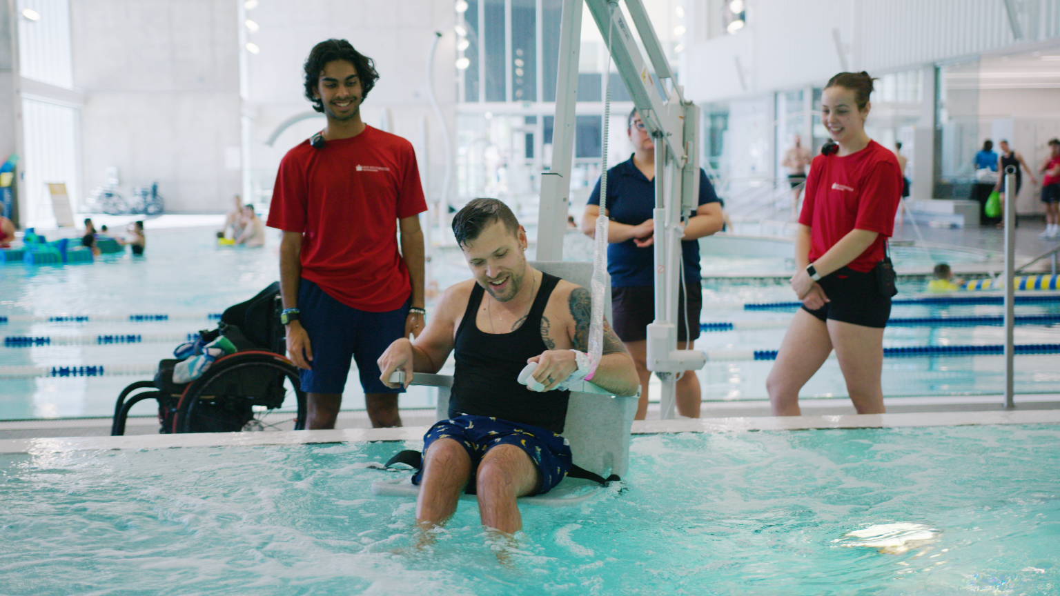 A man in a swimsuit using the transfer device to move from his wheelchair to the pool. 