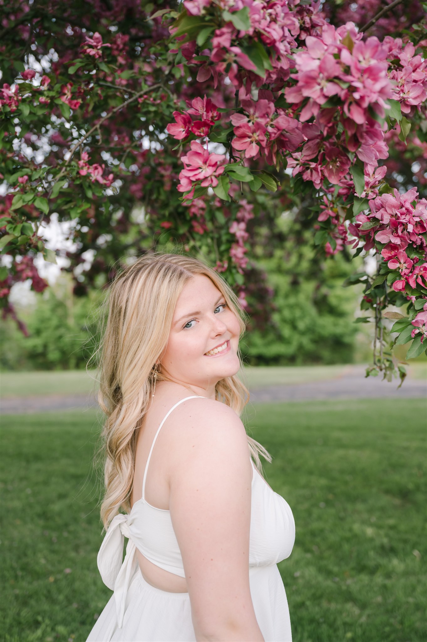 A photo of Abby wearing a white dress in front of cherry blossoms smiling brightly at the camera. 