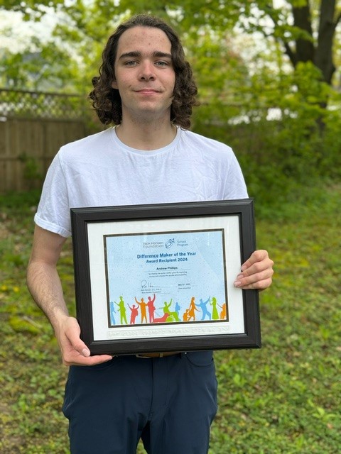 Andrew stands in his back yard holding his framed award