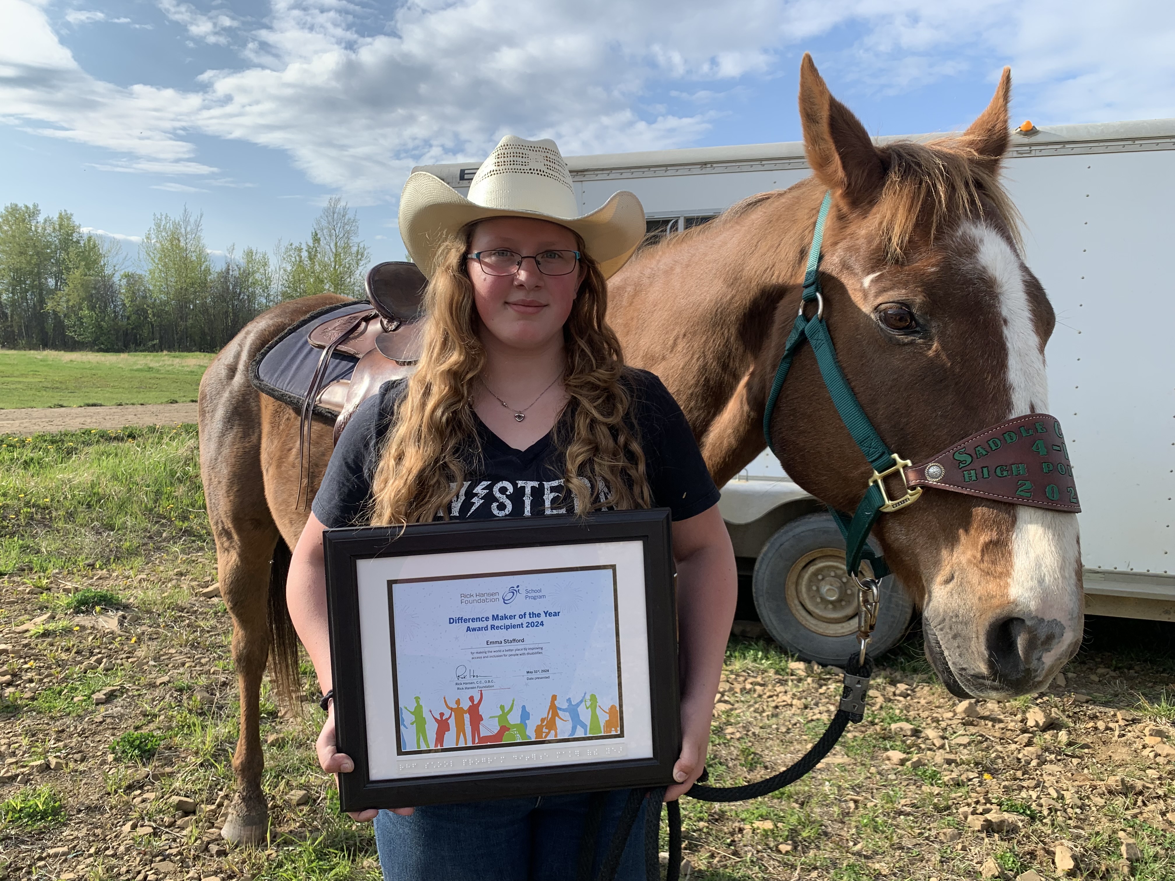 Emma holds her framed award while standing in front of a horse