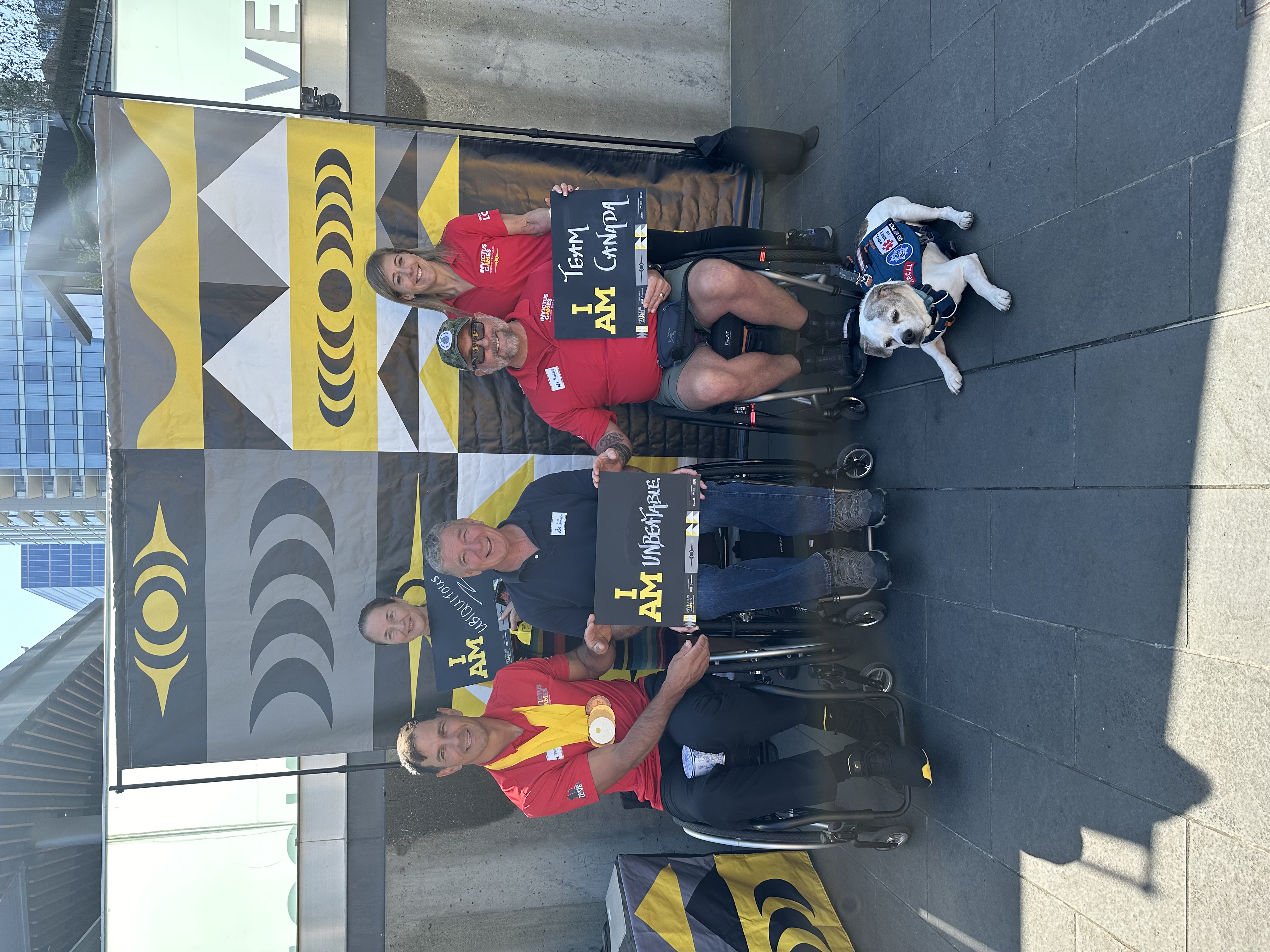 Rick as part of an event promoting the 2025 Invictus Games at the Vancouver Convention Centre. Rick is holding a sign that says I AM Unbeatable. There are four others in the shot, smiling brightly. L-R: Major (Retired) Patrick Lewis, MLA Susie Chant, Rick, Robert Pullen and Assunta Aquino