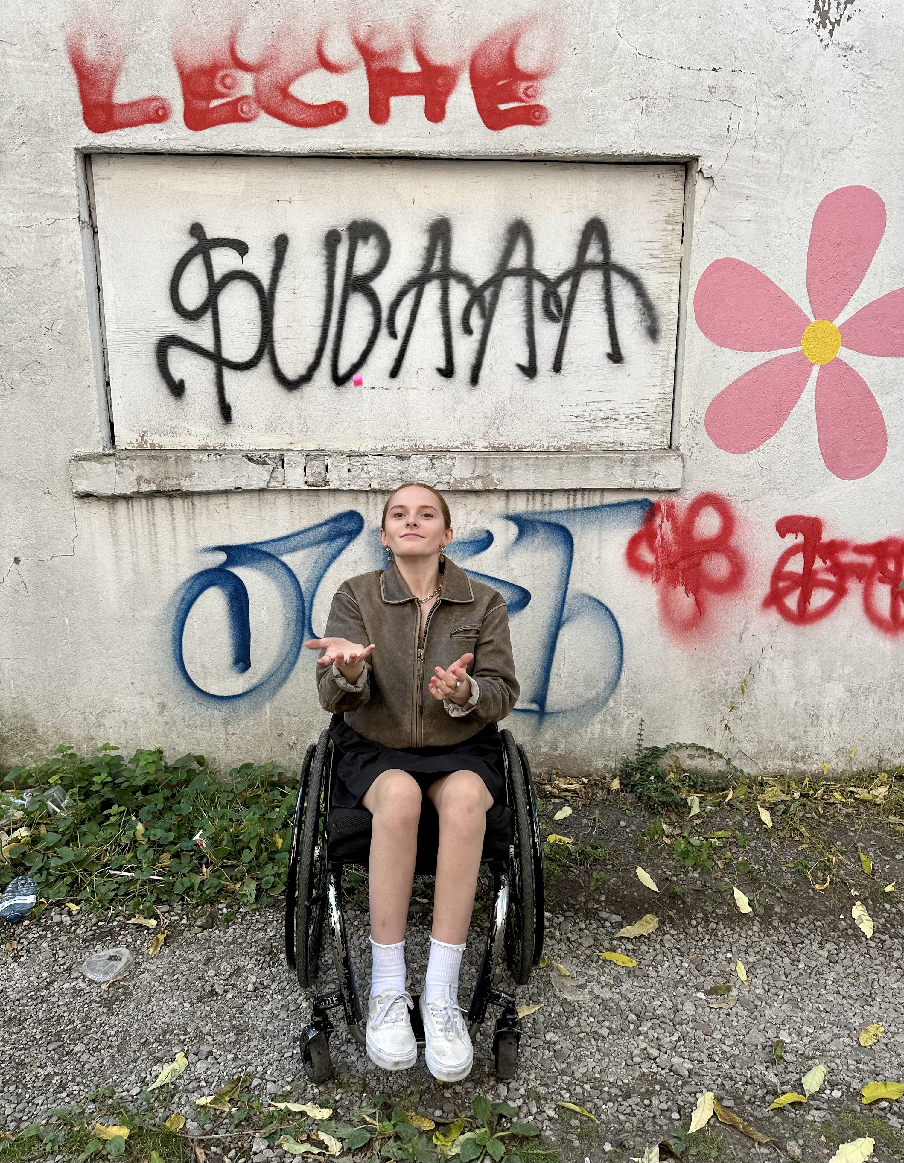 Emily in front of a painted wall with flowers and grafitti style lettering. 