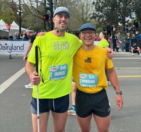 Josh Kwinecki with a friend at a running marathon. Both of them are wearing blue hats and bright yellow shirts and black shorts.