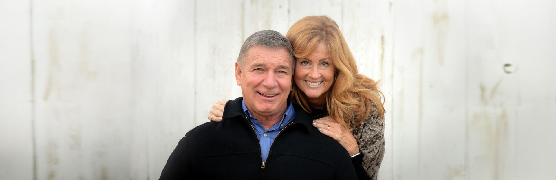 Rick and Amanda Hansen pose and smile together in front of a grey backdrop.