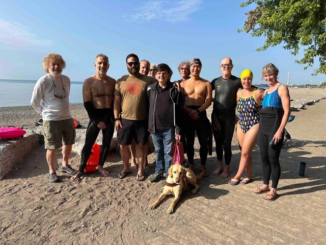 Ripple Effect swimmers stand in the middle of the sand with RHF Ambassador and Paralympic swimmer, Robert Hampson.