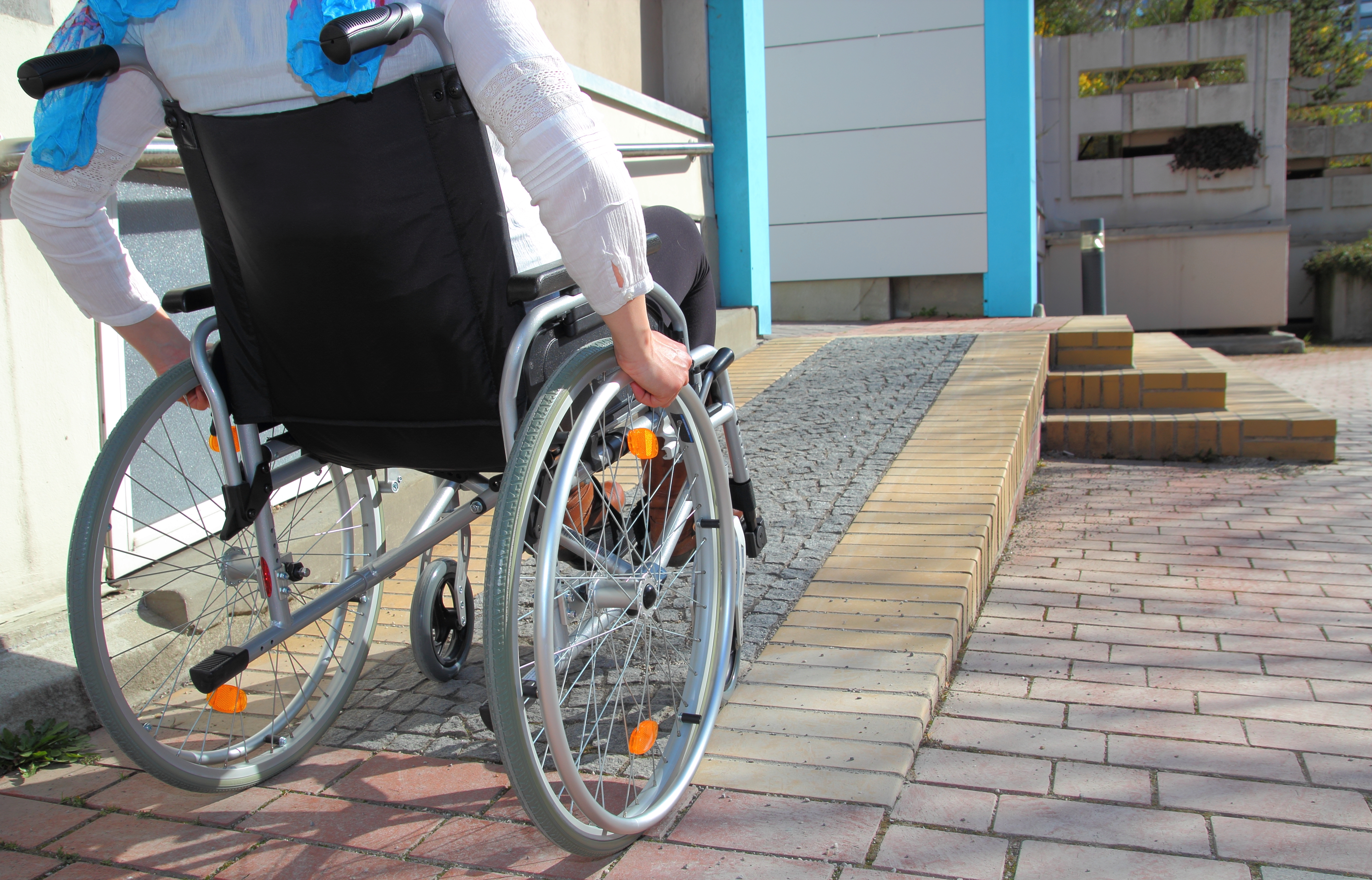 Individual using a wheelchair rolling up a ramp into an establishment. 