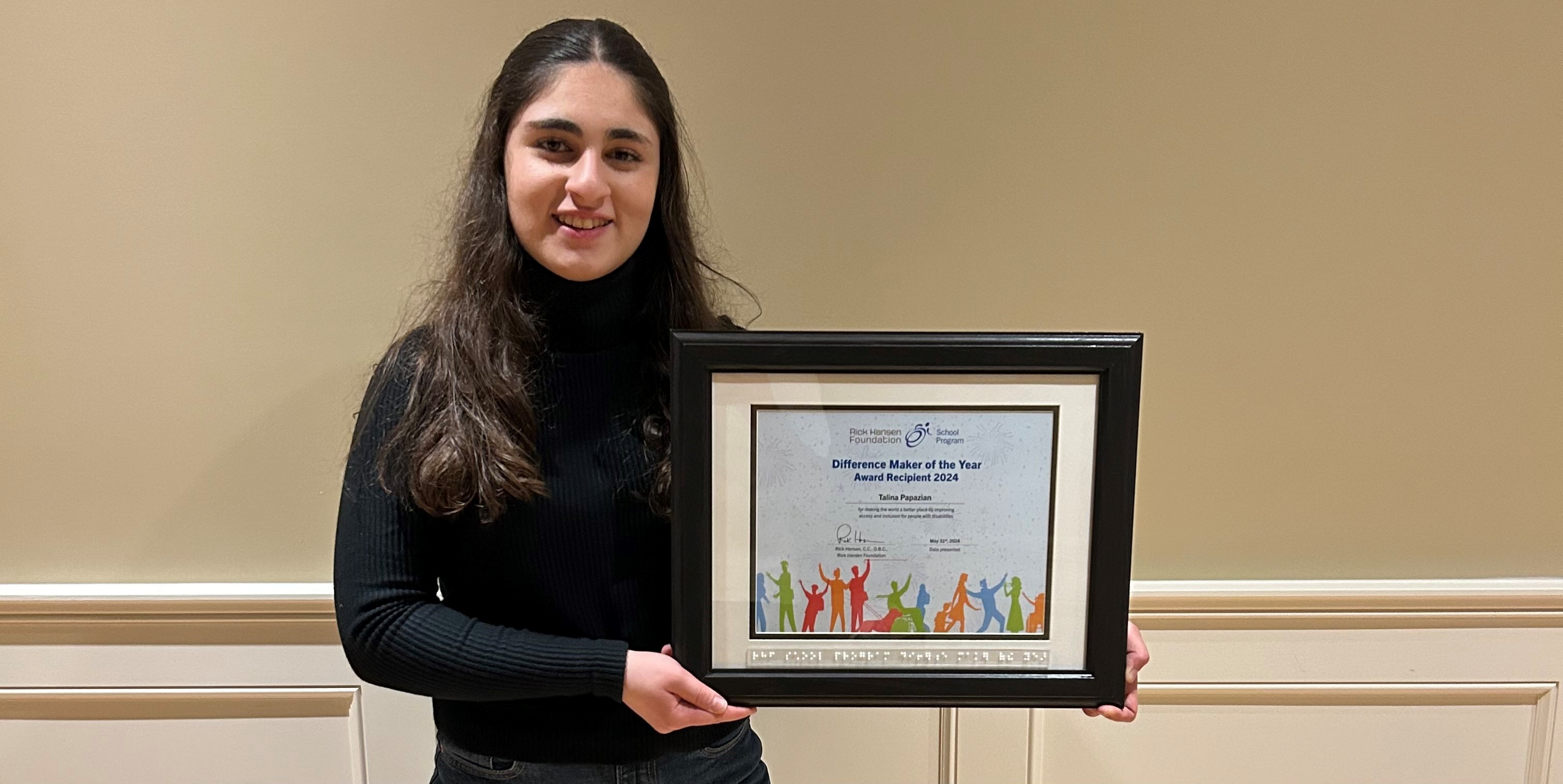 Talina Papazia stands holding her framed Difference Maker of the Year Award