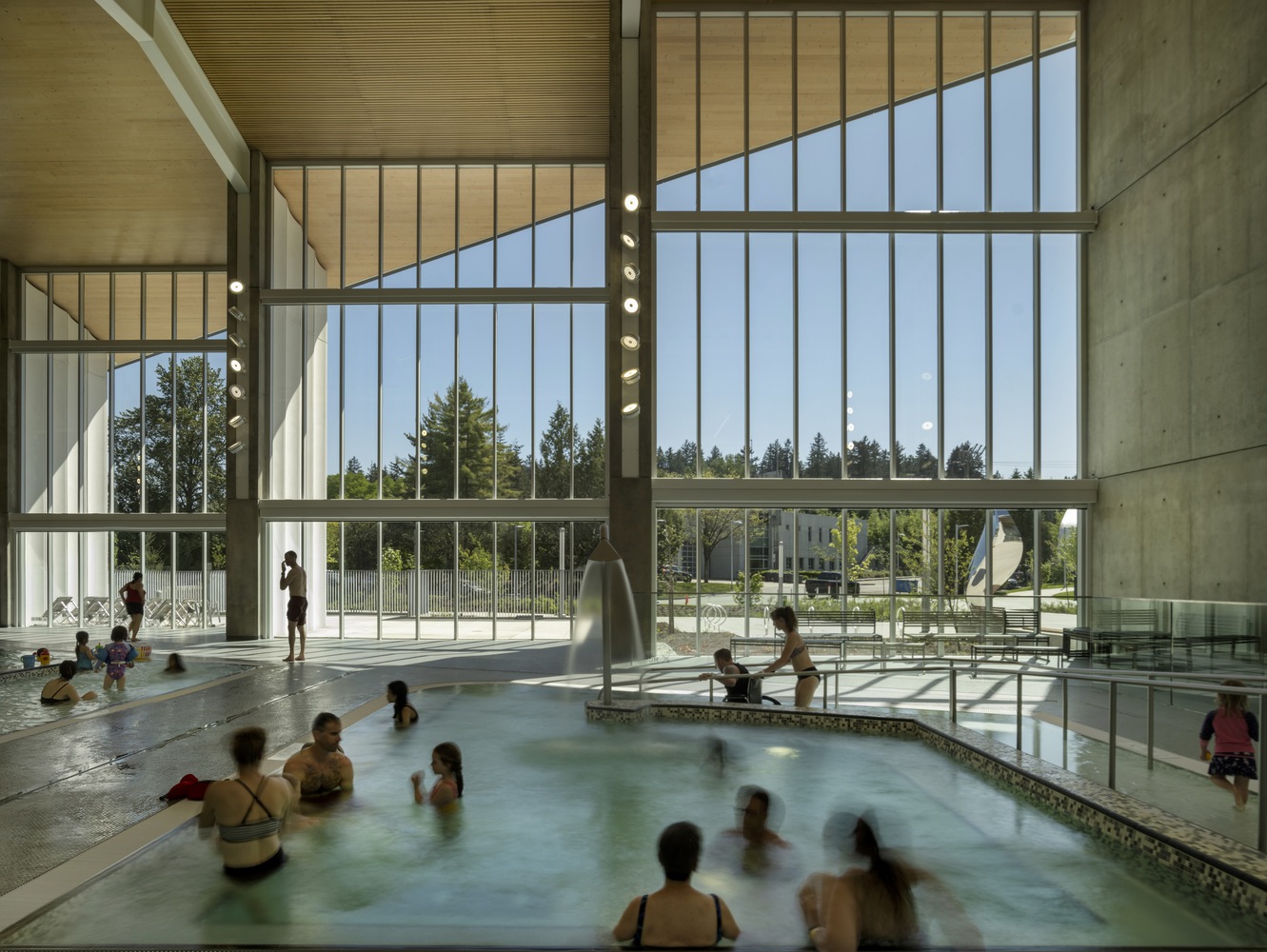 An interior image of the pool facility. In the image many people of ages and abilities are utilizing the space. 