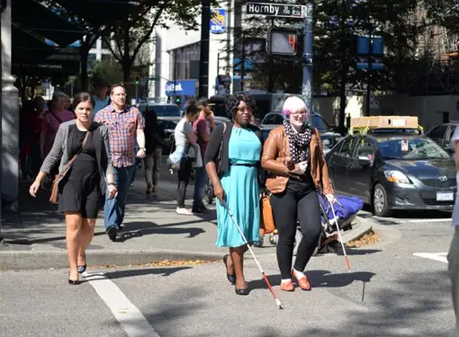 Two people with disabilities cross the street in downtown Vancouver