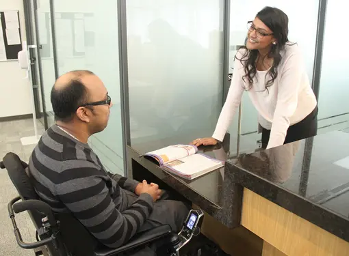 wheelchair user and woman converse at a universal height counter in a business