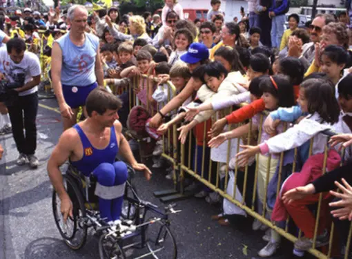 Rick Hansen on his wheelchair wheeling past youth supporters trying to high-five him during his Man In Motion World Tour.