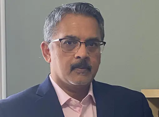 Mathur Variem who has short salt and pepper hair and a moustache. He has glasses and is wearing a darks suit jacket and pink button up shirt.
