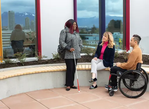 Three people outside talking next to a building. They each have a different disability 