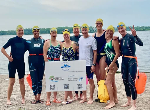 Nine Ripple Effect swimmers are standing by the water while holding a large sign of funds.