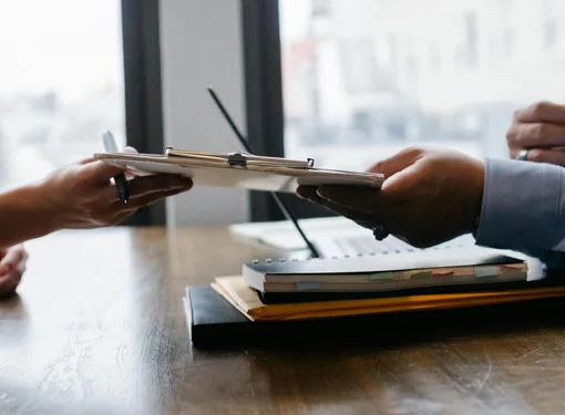 Two people are sitting across the table and passing a chart with a job application on top.