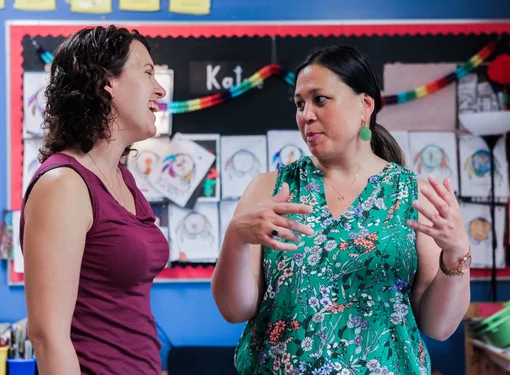 Two women have an animated conversation in a classroom