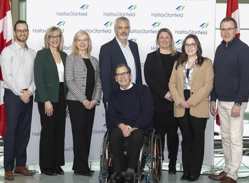 A photo of eight individuals involved in the project standing in front of a Halifax Stanfield International Airport  backdrop. 