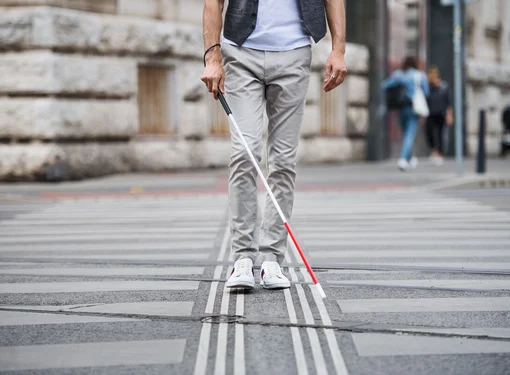 Person uses red tipped white cane to navigate a city street