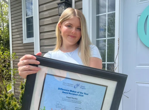 Abby standing in front of a house holding her Difference Maker of the Year award