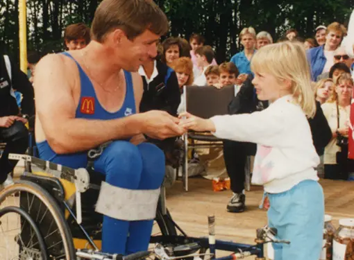 A little girl gives Rick Hansen a donation at a McDonald's restaurant during the Man in Motion World Tour