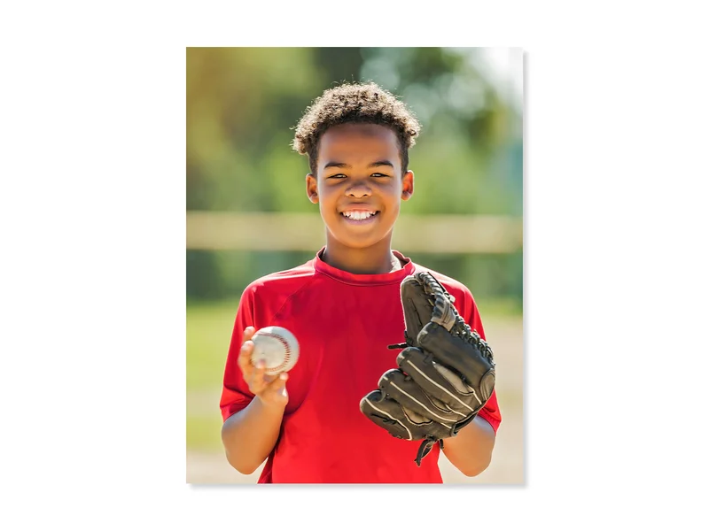 Student wearing a red sport jersey, holding a baseball and smiling.