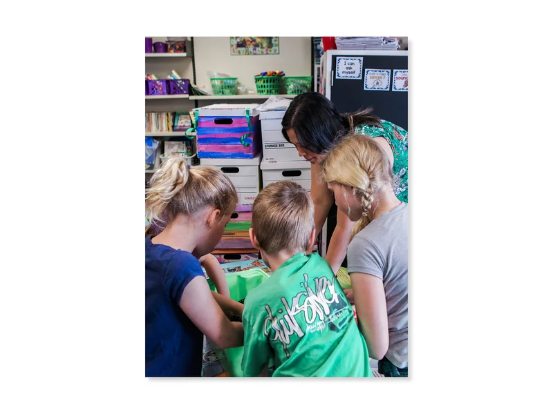 A teacher and three elementary students gather around a classroom table.