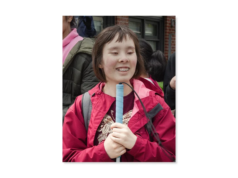 Woman with a pink jacket holding a white cane in front of her.