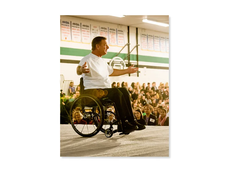 Rick Hansen speaks on stage in front of a large school audience.