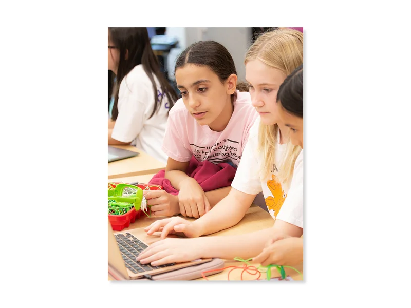 Three girls in a classroom work together at a laptop. 