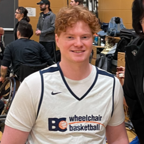 Red haired young man in athletic basketball uniform using a wheelchair, cheery